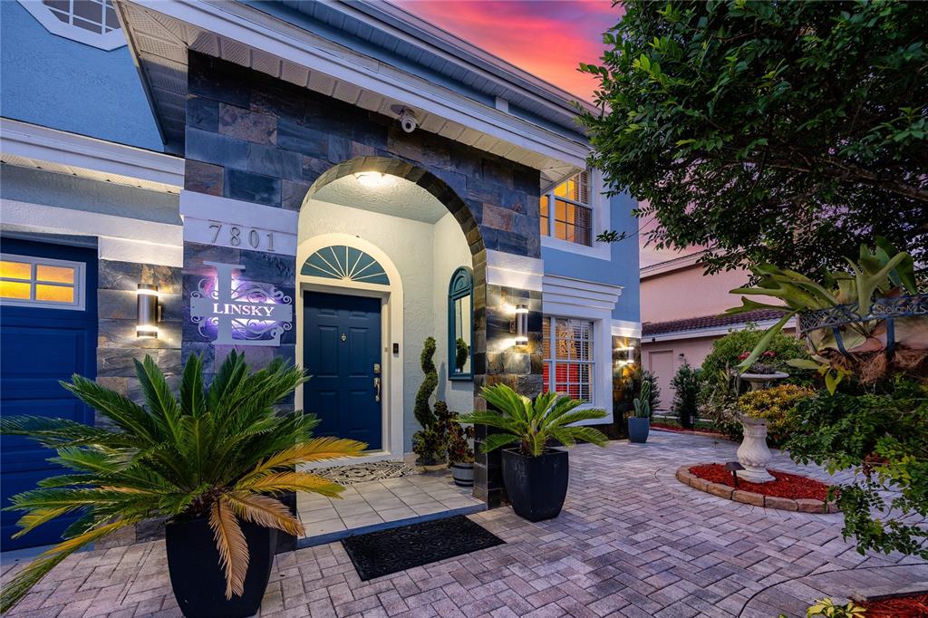 The exterior of a two-story house features a stone-accented arched entryway and a paved courtyard — 7801 HAMLET DRIVE, NEW PORT RICHEY, FL