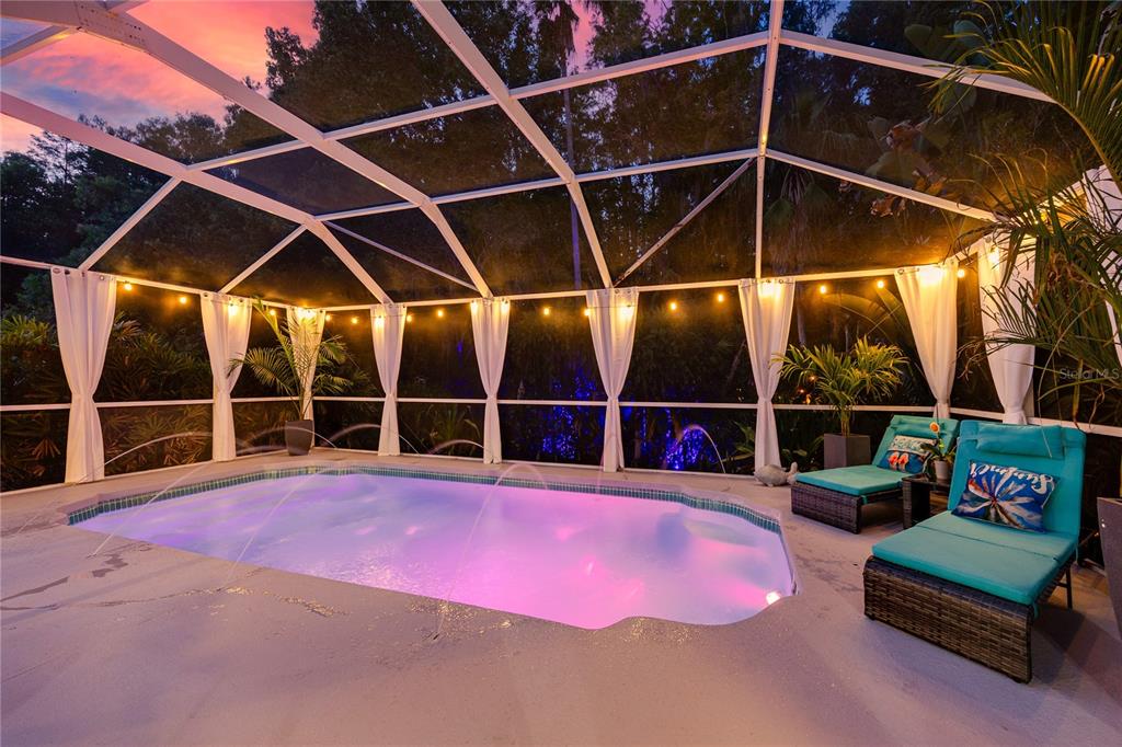 A screened-in swimming pool area at dusk with lounge chairs and string lights — 7801 HAMLET DRIVE, NEW PORT RICHEY, FL