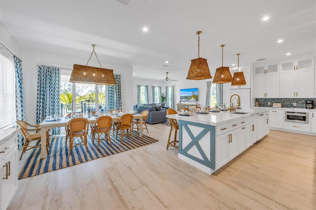 An open-concept kitchen and dining area features a large island, wicker lighting, and wood flooring — 518 SPRING AVENUE, ANNA MARIA, FL