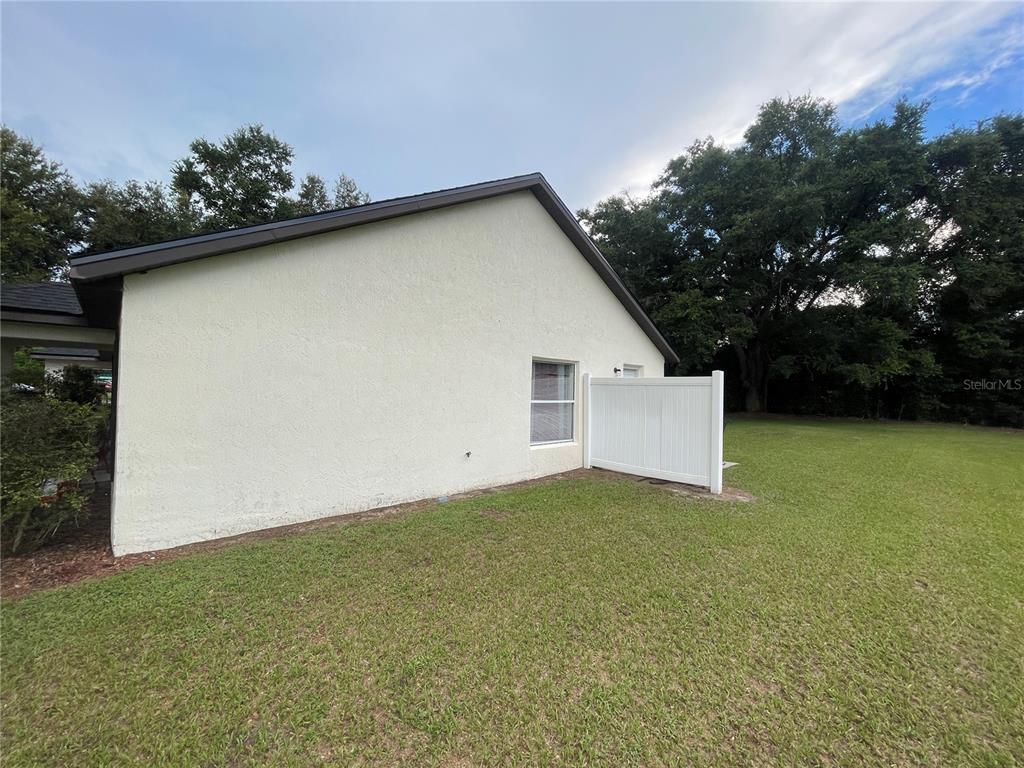 The exterior side view of a house features a white stucco wall, a window, and a fence — 1783 108TH LANE UNIT A & B, OCALA, FL
