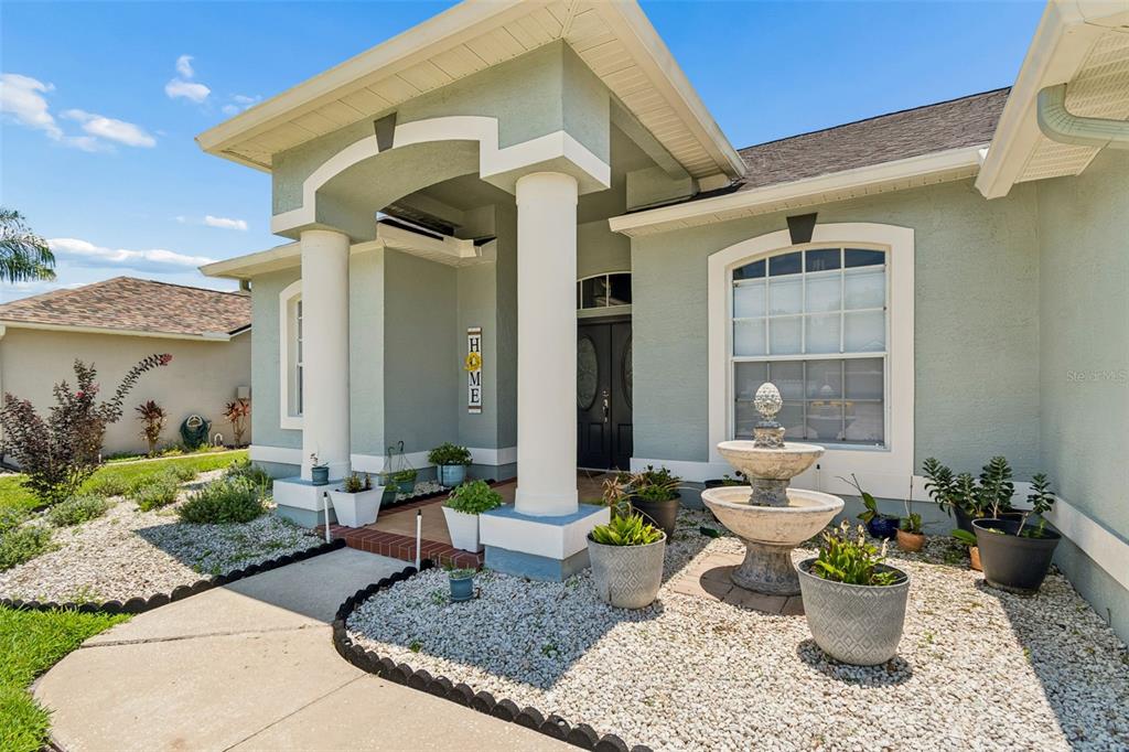 A light green house exterior features a covered entryway with white columns and a fountain — 2154 GROUND SQUIRREL DRIVE, NEW PORT RICHEY, FL