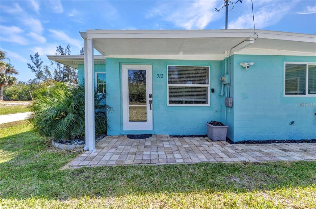 The exterior of a turquoise-painted building features a paved patio, a glass door, and windows — 312 DARST AVENUE, PUNTA GORDA, FL