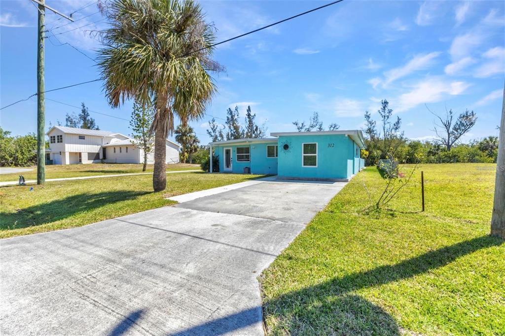 A bright blue, single-story house with a concrete driveway and a palm tree in front — 312 DARST AVENUE, PUNTA GORDA, FL