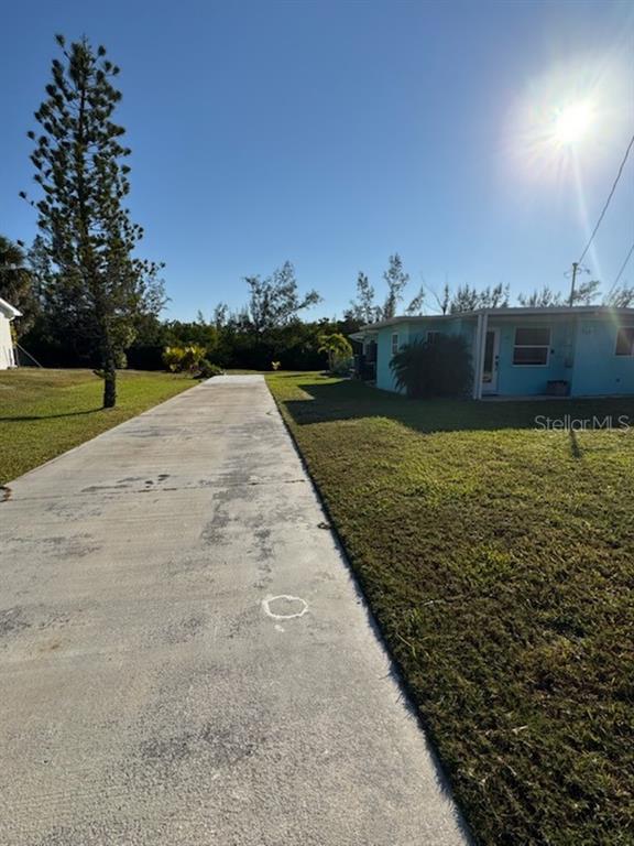 A long concrete driveway leads toward a light blue house under a bright sun — 312 DARST AVENUE, PUNTA GORDA, FL