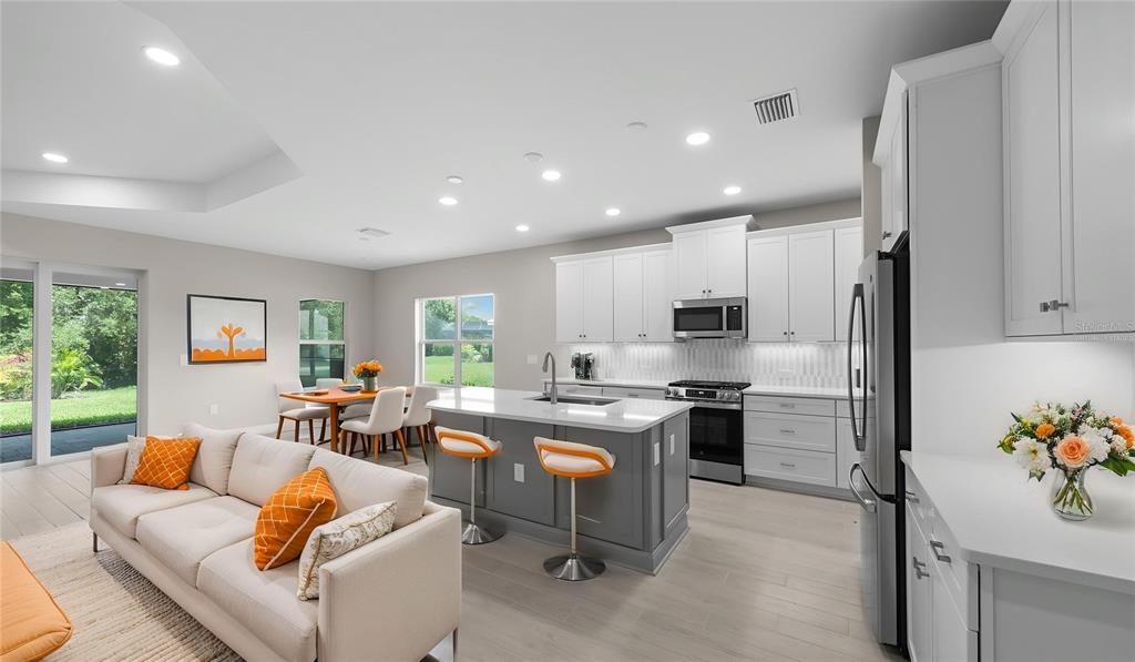 A modern open-concept kitchen and living area featuring white cabinetry, a gray island, and seating — 3099 HERITAGE PINES DRIVE, FORT MYERS, FL