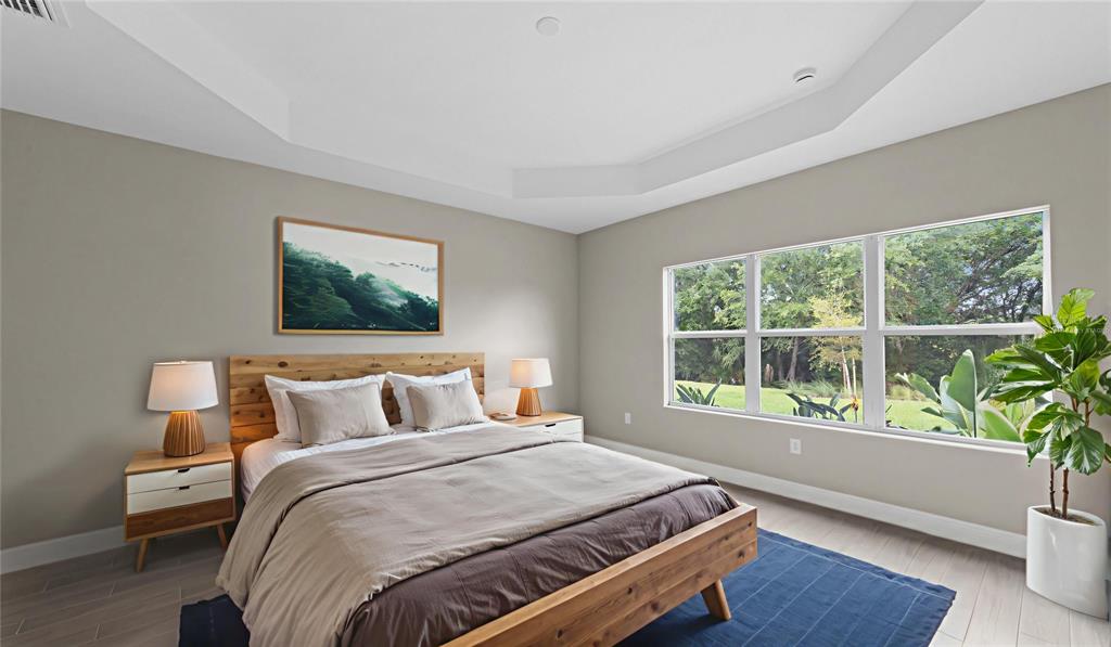 A bedroom with a wooden bed frame, two nightstands, and large windows overlooking trees — 3099 HERITAGE PINES DRIVE, FORT MYERS, FL