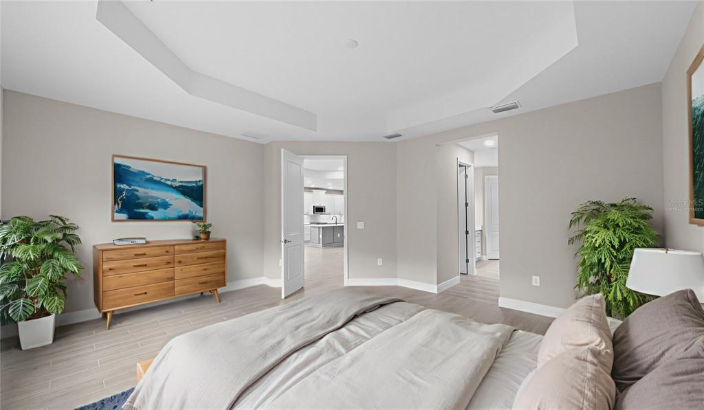 A bedroom with light wood flooring, a tray ceiling, and a view into a kitchen — 3099 HERITAGE PINES DRIVE, FORT MYERS, FL
