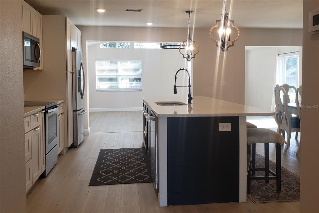 A kitchen features a dark blue island, white cabinets, stainless steel appliances, and wood flooring — 404 KING LOUIS COURT, SEFFNER, FL
