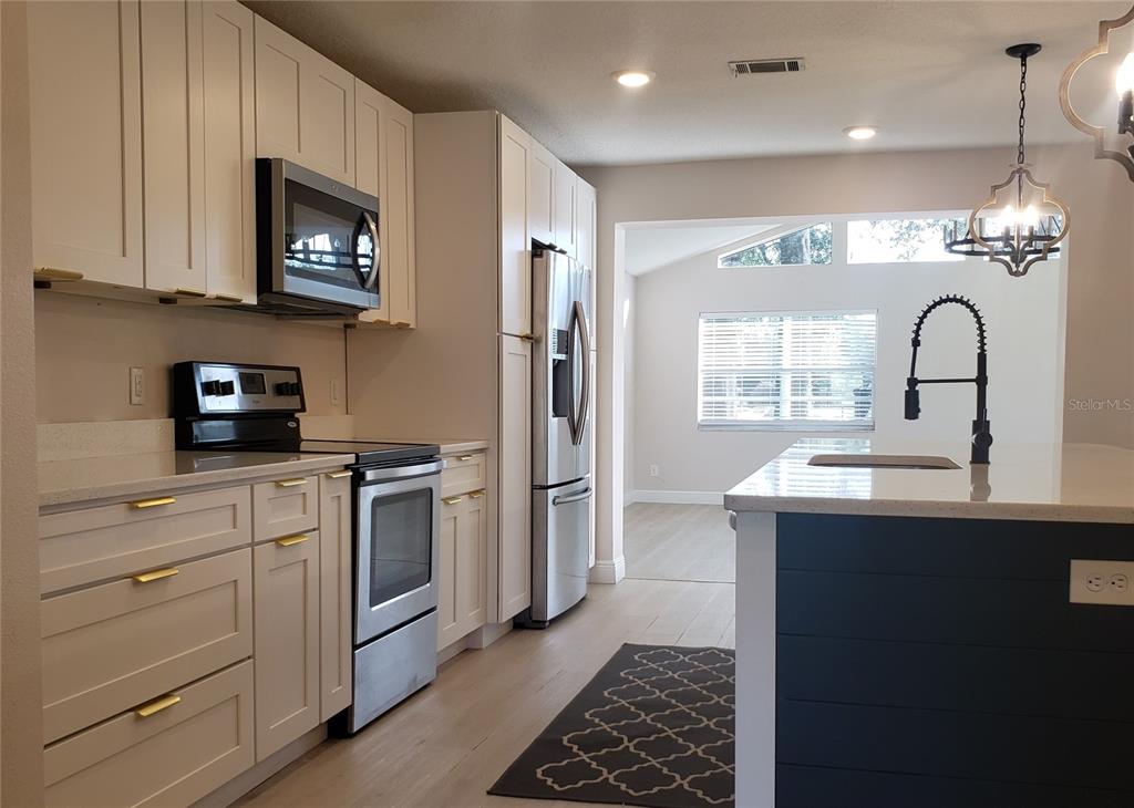 A modern kitchen features white cabinets, stainless steel appliances, and a dark blue kitchen island — 404 KING LOUIS COURT, SEFFNER, FL