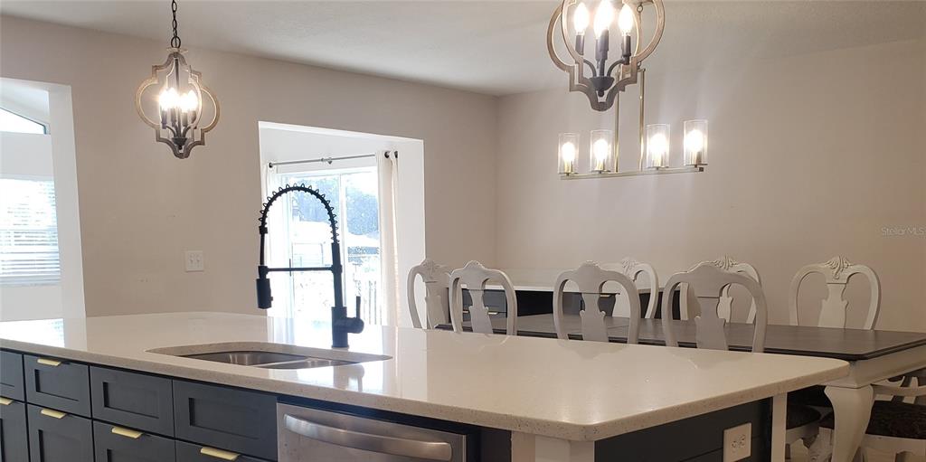 A kitchen island with a sink and dark cabinets sits before a dining area — 404 KING LOUIS COURT, SEFFNER, FL