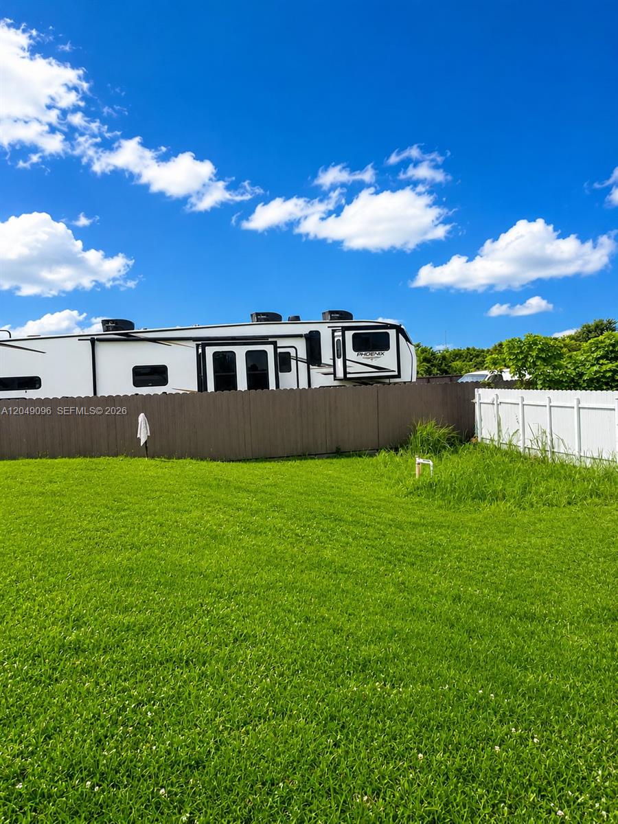 A white recreational vehicle is parked behind a brown wooden fence in a grassy yard — 2903 19TH ST SW, Lehigh Acres FL 33976, LEHIGH ACRES, FL