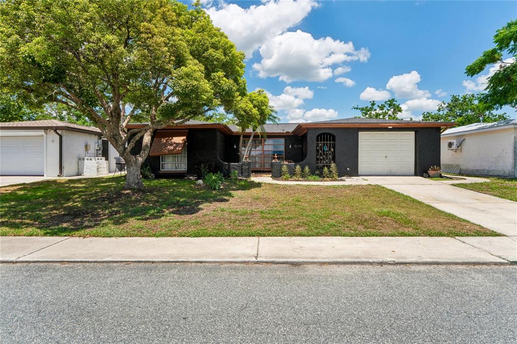 A single-story house with a black exterior, a white garage door, and a large tree — 10120 GLEN MOOR LANE, PORT RICHEY, FL