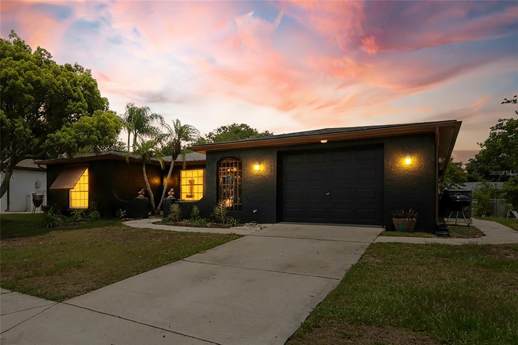 A dark-painted single-story house with a garage and a concrete driveway at sunset — 10120 GLEN MOOR LANE, PORT RICHEY, FL