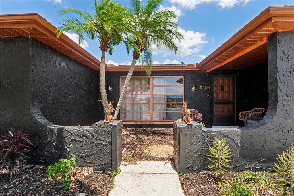A black stucco house exterior features a front courtyard with two palm trees and statues — 10120 GLEN MOOR LANE, PORT RICHEY, FL
