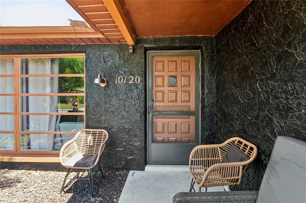A front porch features a dark textured wall, a wooden door, and two wicker chairs — 10120 GLEN MOOR LANE, PORT RICHEY, FL