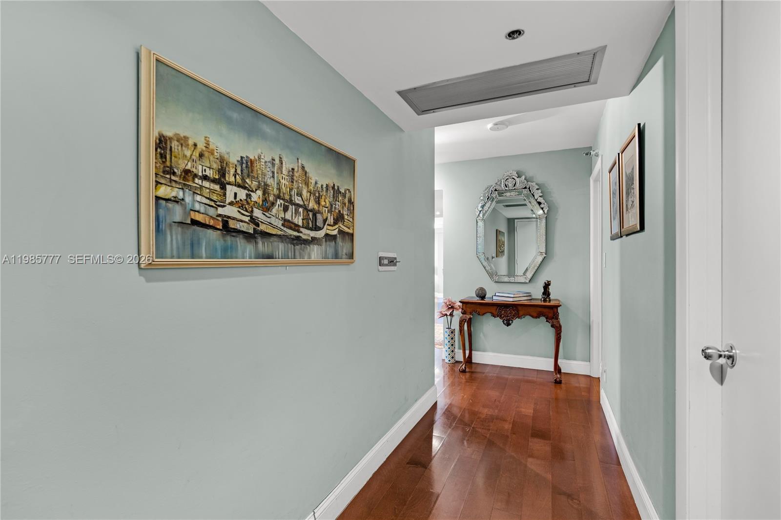 A hallway with light blue walls, hardwood floors, a large painting, and a console table — 2025 Brickell Ave # 1703, Miami FL 33129, MIAMI, FL