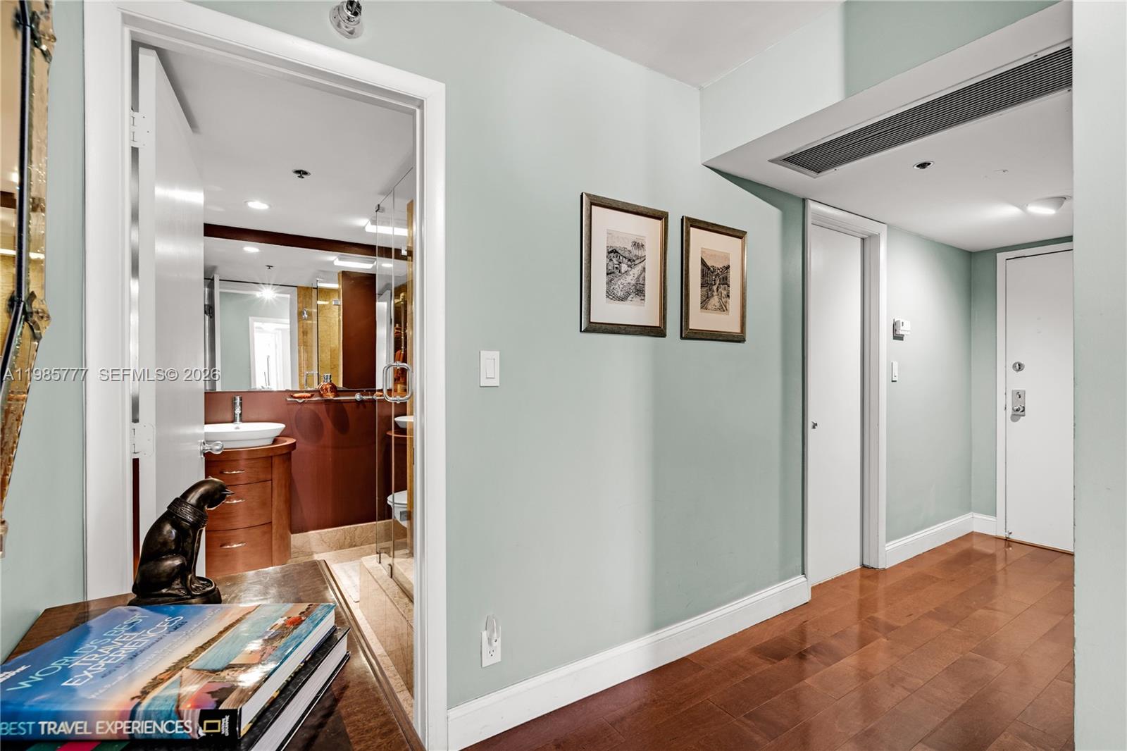 A hallway with hardwood floors leads to a bathroom with a vanity and glass shower — 2025 Brickell Ave # 1703, Miami FL 33129, MIAMI, FL