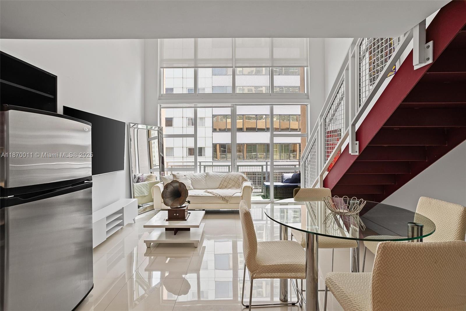 A modern living and dining area features a red staircase, floor-to-ceiling windows, and tile flooring — 253 NE 2 ST # 626, Miami FL 33132, MIAMI, FL