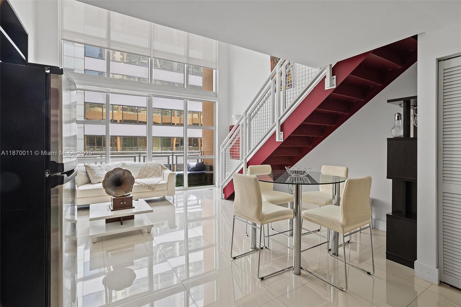 A modern living and dining area features a red staircase, floor-to-ceiling windows, and tile flooring — 253 NE 2 ST # 626, Miami FL 33132, MIAMI, FL