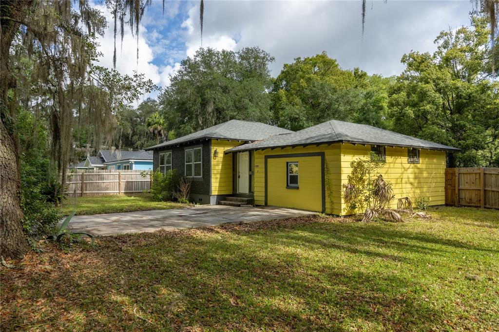 A yellow single-story house with a gray roof and a concrete driveway sits on grass — 1334 NE 1ST AVENUE, GAINESVILLE, FL