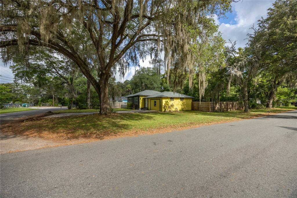 A yellow house with a gray roof sits on a corner lot under large trees — 1334 NE 1ST AVENUE, GAINESVILLE, FL