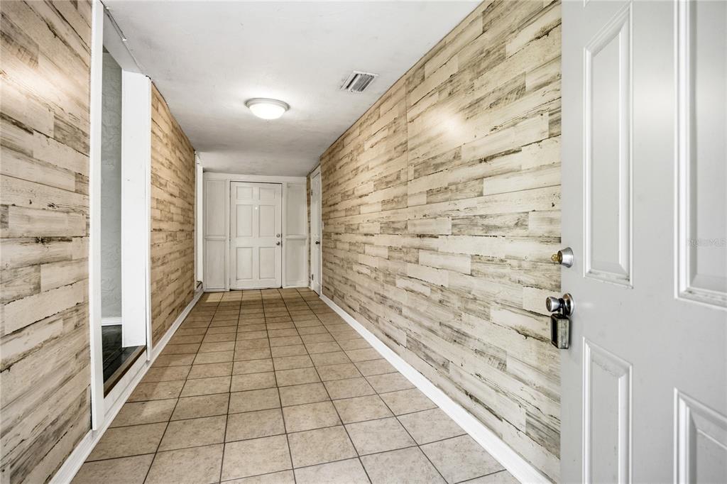 A hallway with light-colored wood-look wall paneling, tiled flooring, and a white door — 1334 NE 1ST AVENUE, GAINESVILLE, FL
