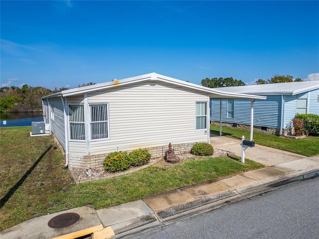 A beige manufactured home with a carport sits next to a pond — 1001 STARKEY ROAD, LOT#355, LARGO, FL