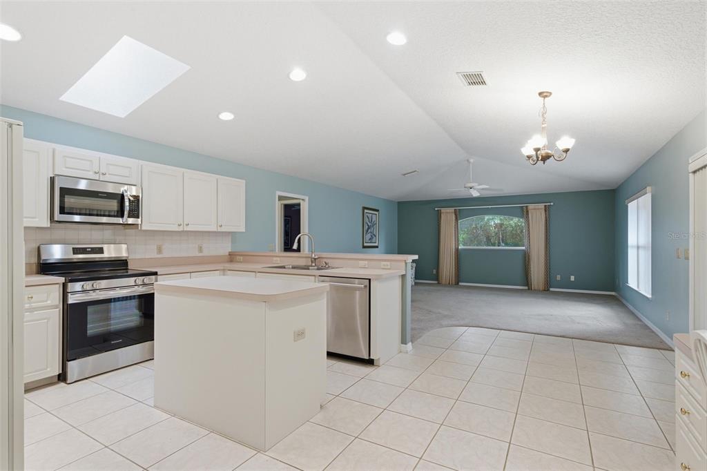 A kitchen with white cabinets and stainless steel appliances opens into a carpeted living area — 1204 N MEDITERRANEAN WAY, INVERNESS, FL