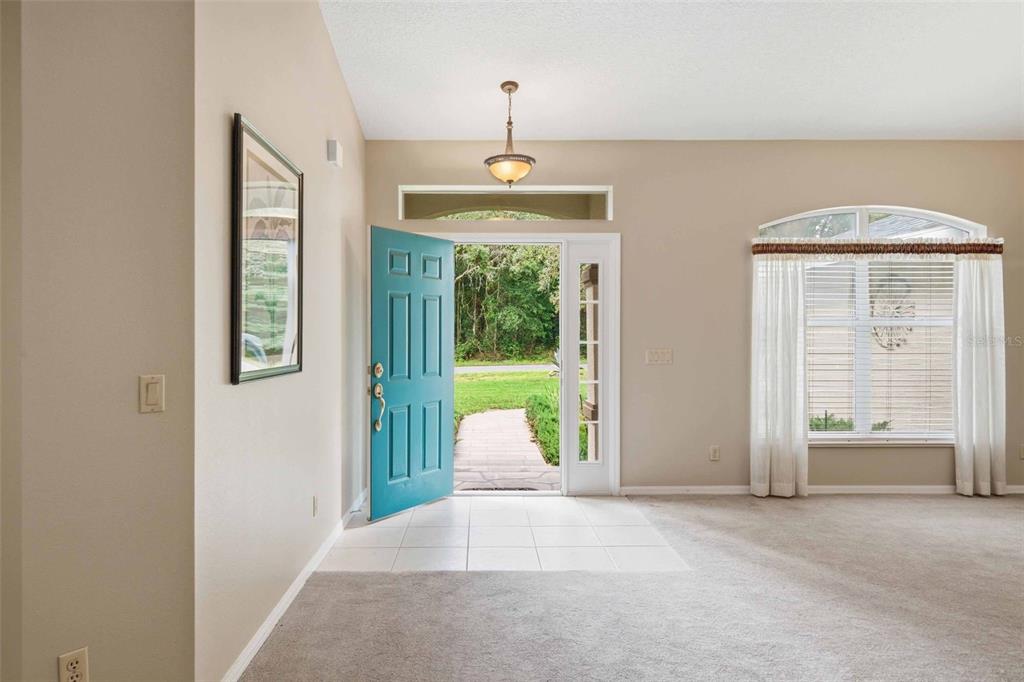 An entryway with a teal front door, tiled floor, and carpeted living area beyond — 1204 N MEDITERRANEAN WAY, INVERNESS, FL