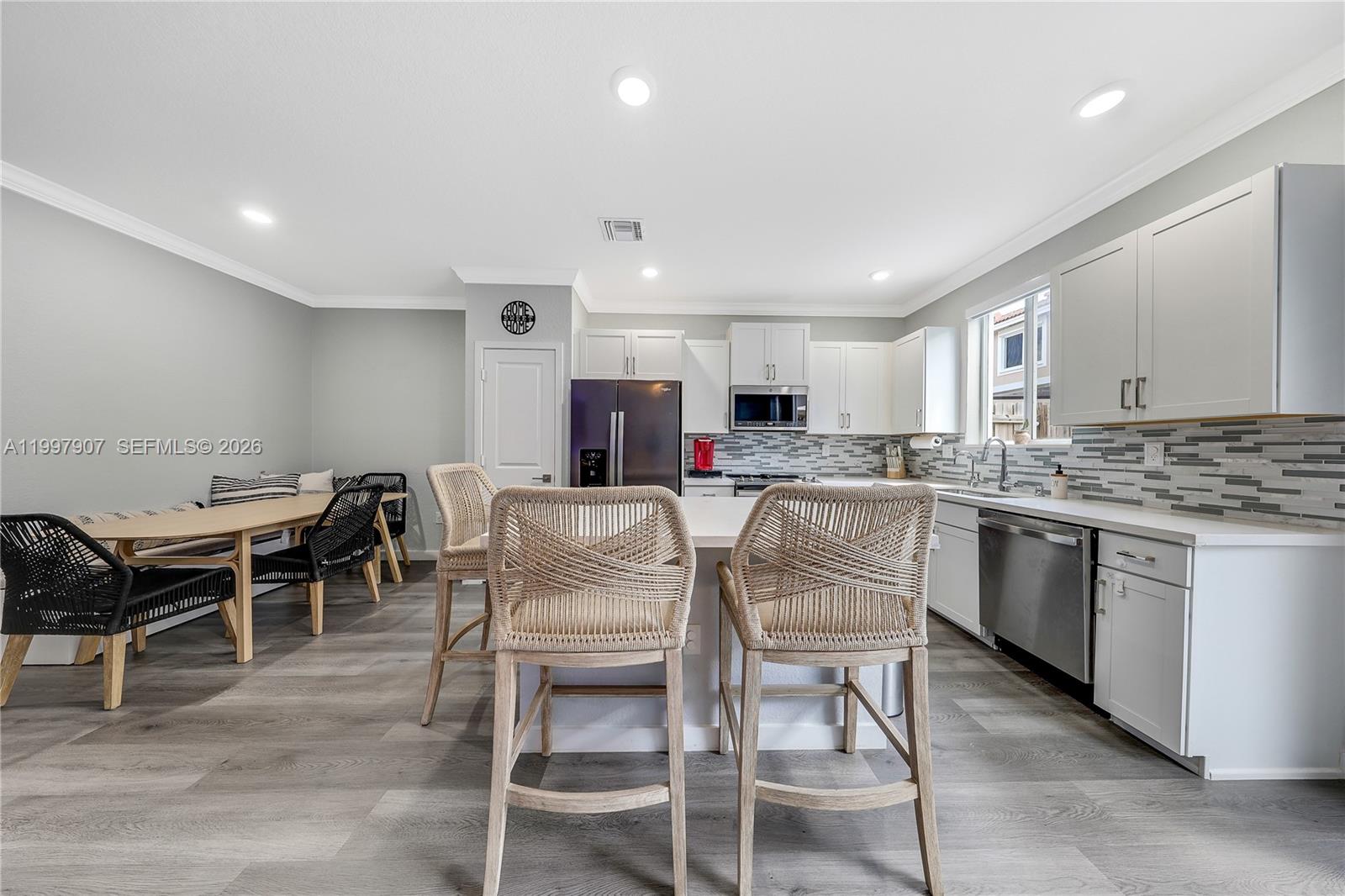 A kitchen features white cabinets, a central island with woven stools, and an adjacent dining area — 1079 SE 23rd Ter, Homestead FL 33035, HOMESTEAD, FL