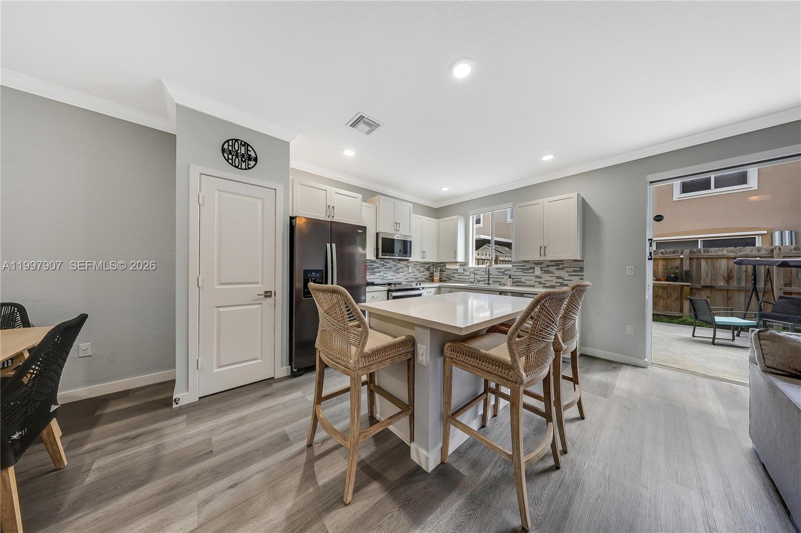 A kitchen features a central island with wicker stools, light cabinetry, and gray flooring — 1079 SE 23rd Ter, Homestead FL 33035, HOMESTEAD, FL