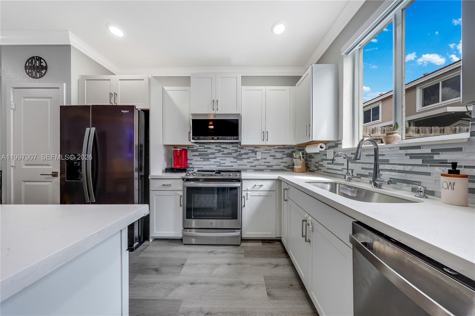 A modern kitchen features white cabinets, stainless steel appliances, a tiled backsplash, and wood-look flooring — 1079 SE 23rd Ter, Homestead FL 33035, HOMESTEAD, FL