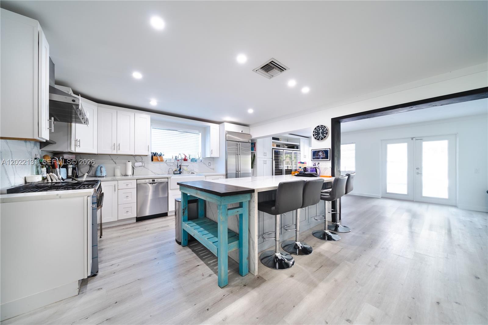 A modern kitchen features white cabinetry, a marble-topped island, and a blue wooden accent table — 1301 Funston St, Hollywood FL 33019, HOLLYWOOD, FL