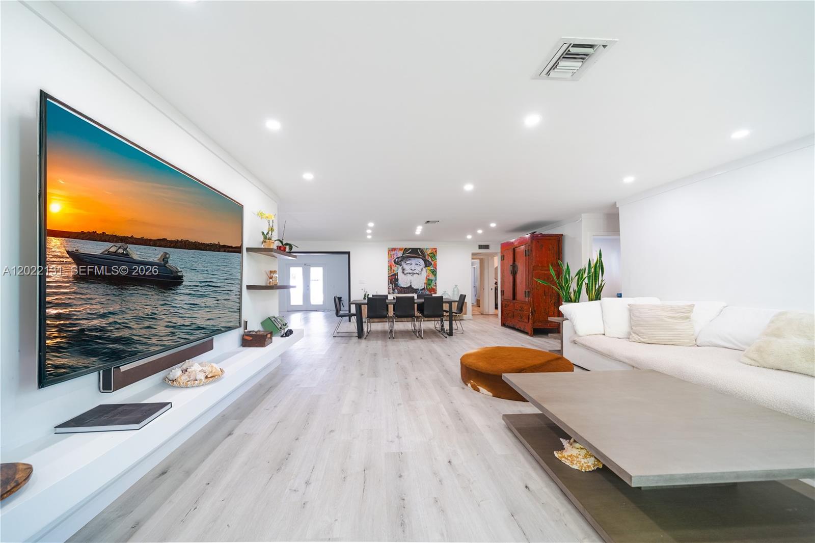 A spacious living and dining area features light wood flooring, a large television, and white walls — 1301 Funston St, Hollywood FL 33019, HOLLYWOOD, FL