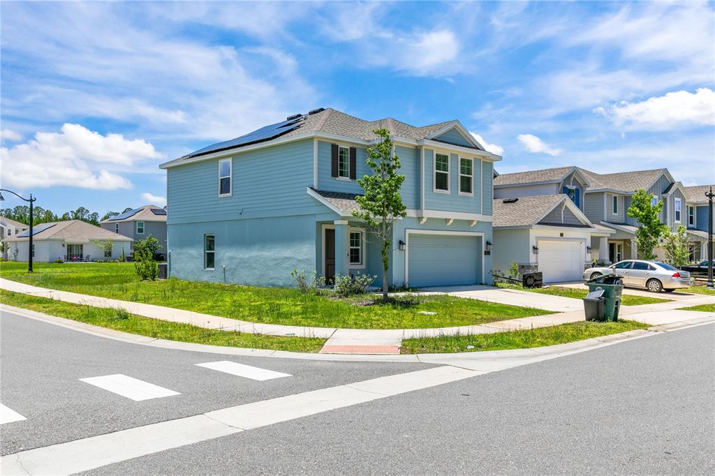 A two-story light blue house with a garage and solar panels sits on a corner — 1127 CABOT CLIFFS DRIVE, DAYTONA BEACH, FL