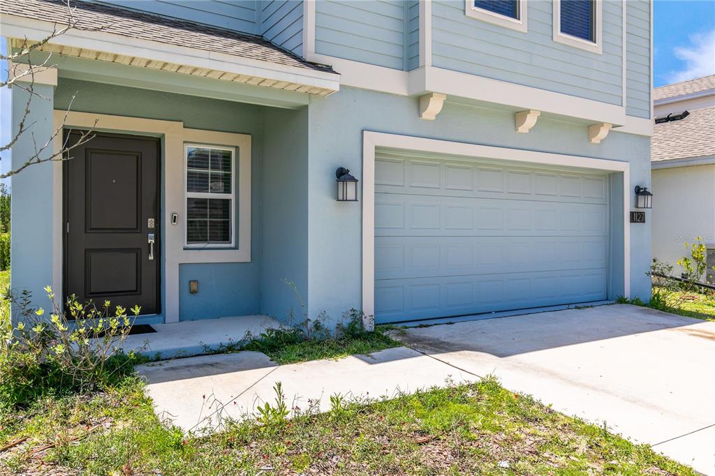 A light blue two-story house features a dark front door and a two-car garage — 1127 CABOT CLIFFS DRIVE, DAYTONA BEACH, FL