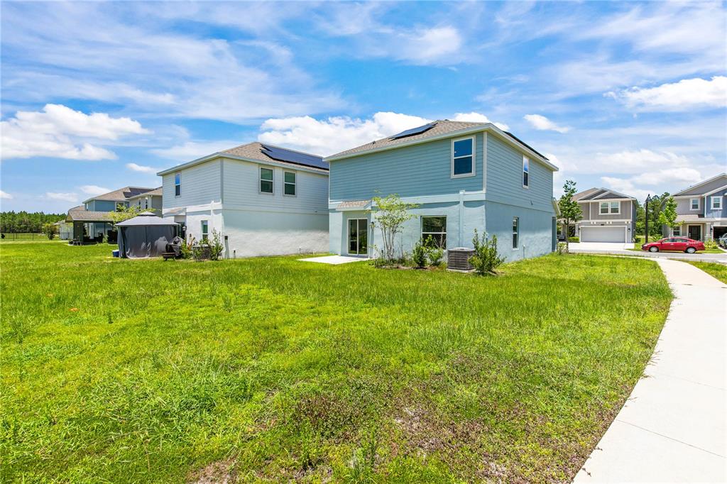 The rear exterior of two light blue two-story houses with solar panels and grassy yards — 1127 CABOT CLIFFS DRIVE, DAYTONA BEACH, FL