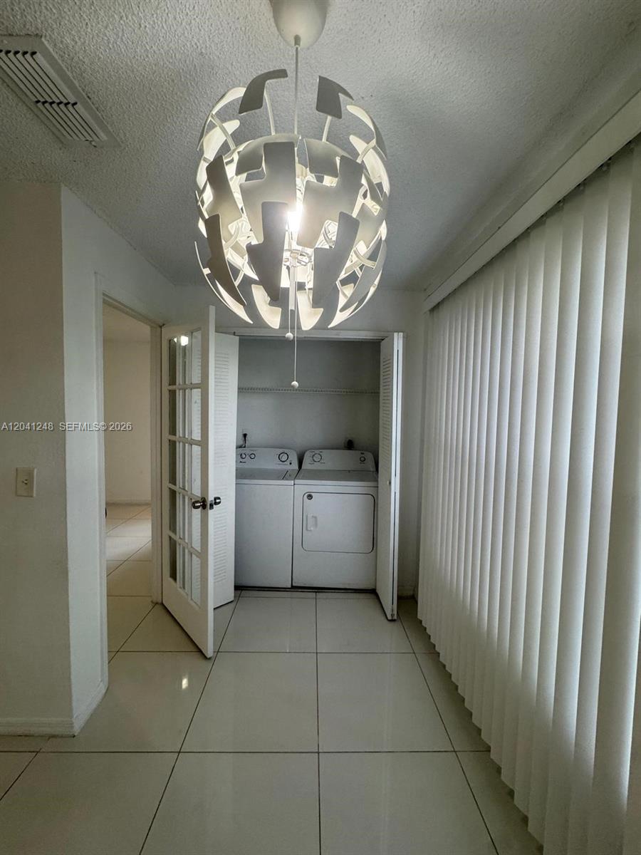 A laundry closet with a washer and dryer sits in a tiled room with a pendant light — MARGATE, FL