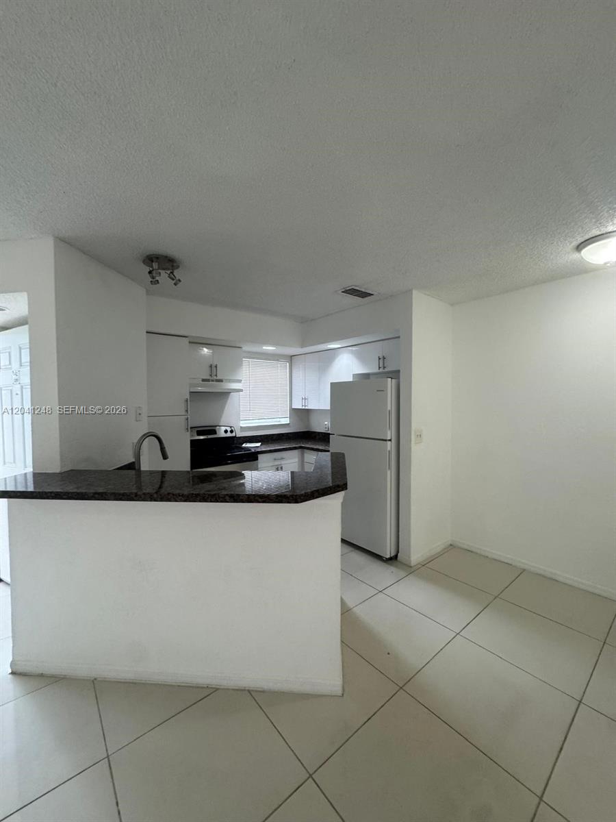 A kitchen features white cabinets, a dark granite countertop, and light-colored floor tiles — MARGATE, FL