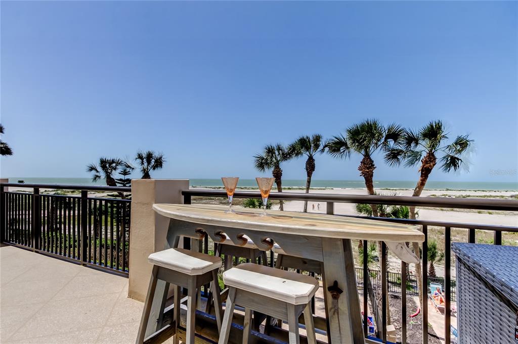 A balcony features a surfboard-shaped table with two stools overlooking a beach and the ocean — 1270 GULF BOULEVARD UNIT 304, CLEARWATER, FL