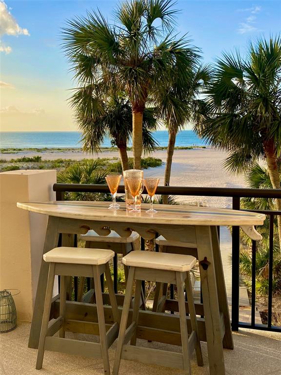 A surfboard-style bar table with two stools sits on a balcony overlooking the beach — 1270 GULF BOULEVARD UNIT 304, CLEARWATER, FL