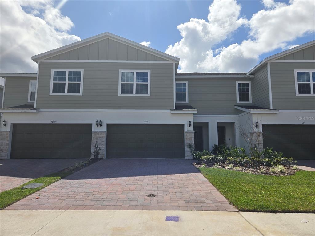 A two-story townhouse with a gray exterior, stone accents, and a paved driveway — 1591 CLOUDY COURT, ST CLOUD, FL