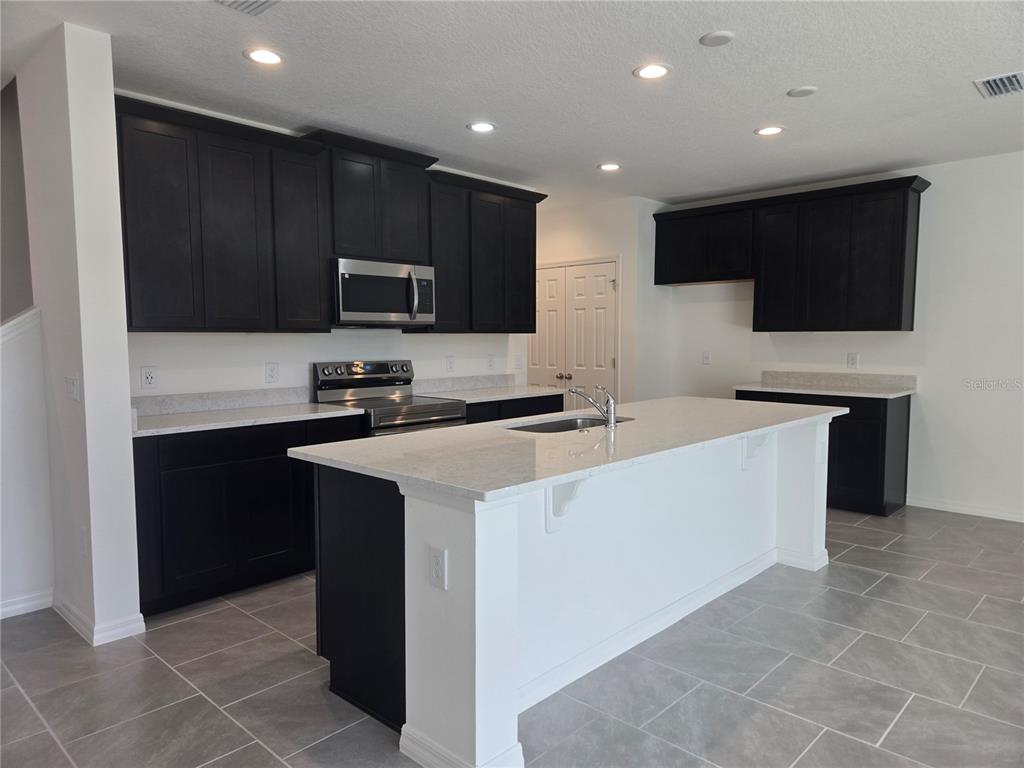 A kitchen features dark cabinets, white countertops, a central island, and gray tile flooring — 1591 CLOUDY COURT, ST CLOUD, FL