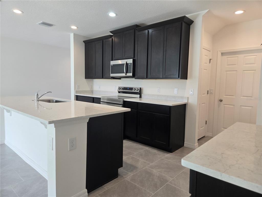 A kitchen features dark wood cabinets, white countertops, stainless steel appliances, and gray tile flooring — 1591 CLOUDY COURT, ST CLOUD, FL