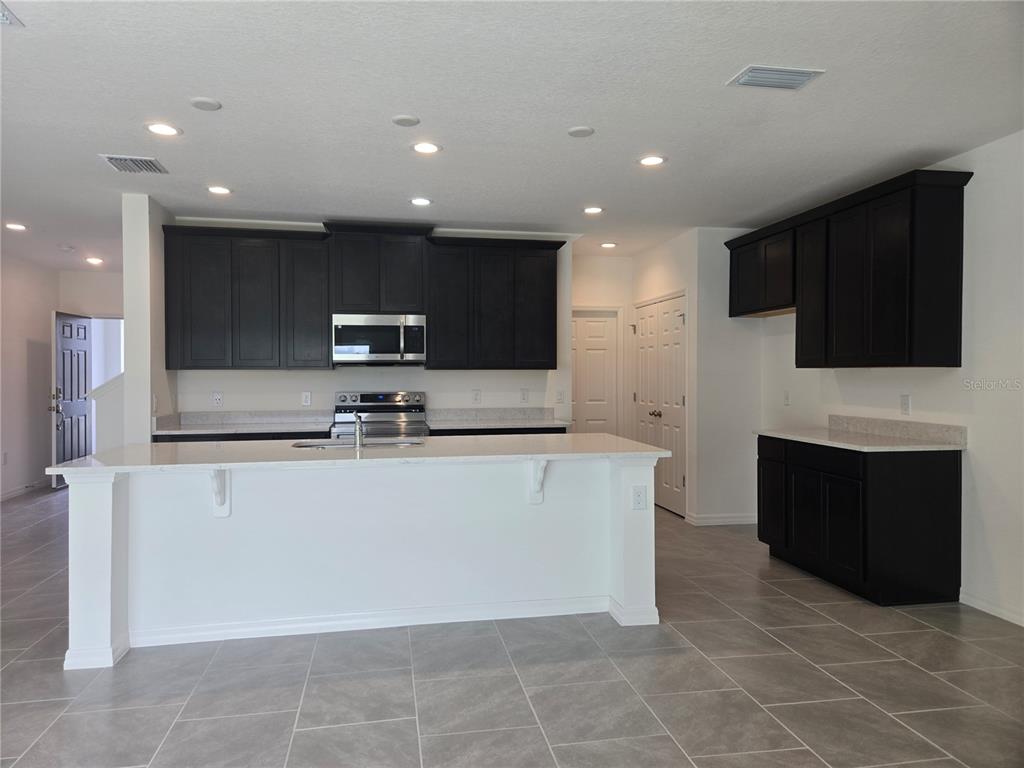 A kitchen features dark cabinetry, white countertops, a central island, and light-colored tile flooring — 1591 CLOUDY COURT, ST CLOUD, FL