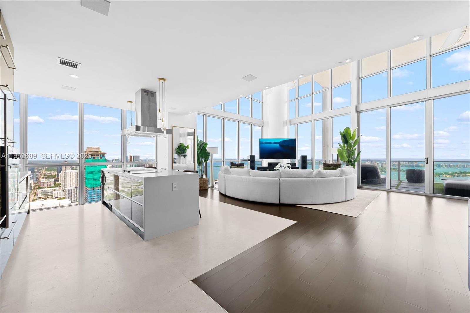 A modern open-concept living area features a white kitchen island, curved sofa, and floor-to-ceiling windows — 1100 Biscayne Blvd # 5706, Miami FL 33132, MIAMI, FL