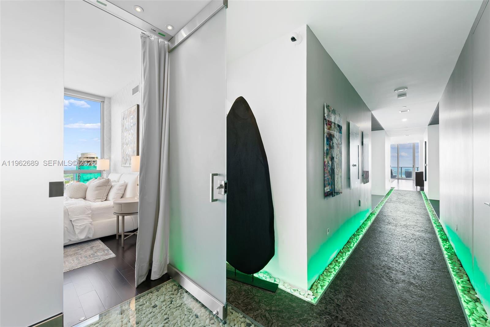 A hallway with green floor lighting and pebble accents leads toward a bedroom and balcony — 1100 Biscayne Blvd # 5706, Miami FL 33132, MIAMI, FL