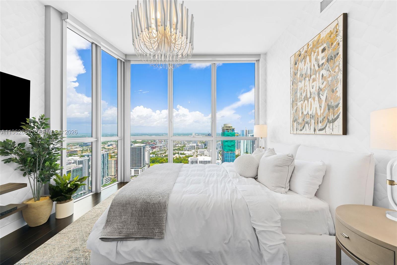 A modern bedroom features floor-to-ceiling windows with a city view and a white bed — 1100 Biscayne Blvd # 5706, Miami FL 33132, MIAMI, FL