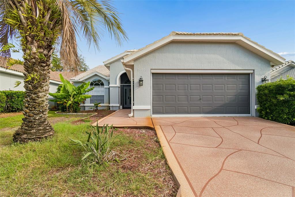 A single-story house with a gray garage, a palm tree, and a patterned concrete driveway — 9376 FRENCH QUARTERS CIRCLE, WEEKI WACHEE, FL