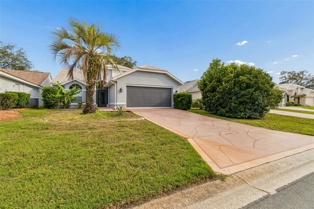 A single-story house with a gray garage door, a palm tree, and a patterned driveway — 9376 FRENCH QUARTERS CIRCLE, WEEKI WACHEE, FL